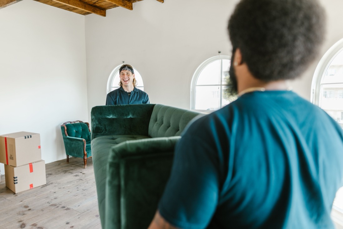 Zwei Umzugshelfer tragen lachend ein Sofa